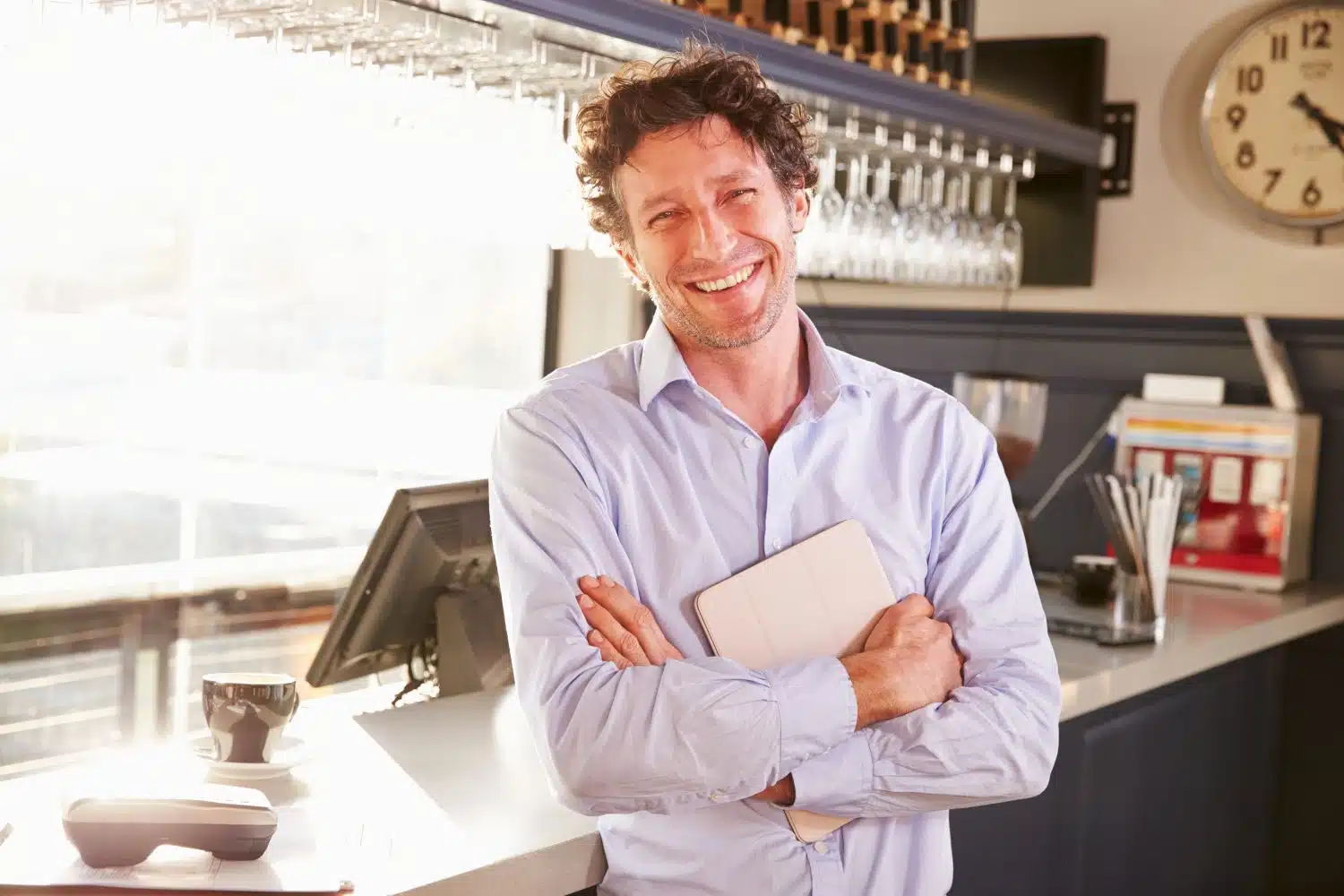 Confident male restaurant owner smiling behind the counter with a tablet in hand