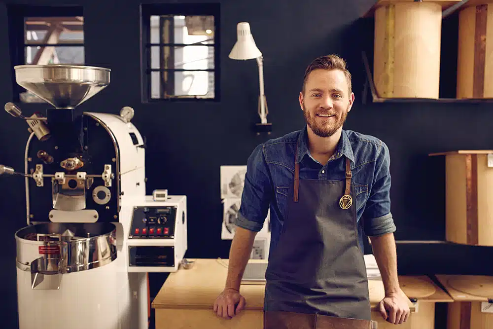 Smiling male coffee roaster standing proudly in his artisan roasting workspace