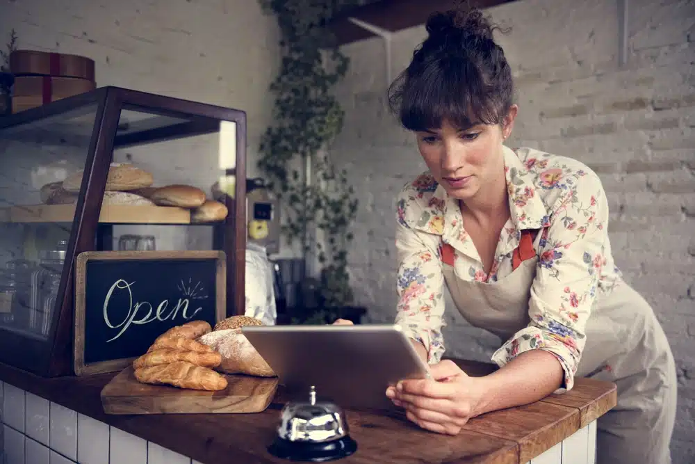 Female bakery owner using tablet behind counter with pastries and open sign